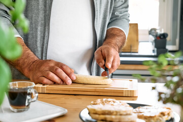 Man making healthy breakfast or brunch, cutting banana for putting it on puffed corn cakes with spread peanut butter. Protein diet healthy eating concept.