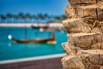 Gordijnen Traditional wooden Dhow boats on blue water in sunny Doha city port with palm trees © g.photobox