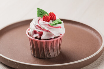 Homemade cupcake decorated with cream and figure chocolate on ceramic plate.