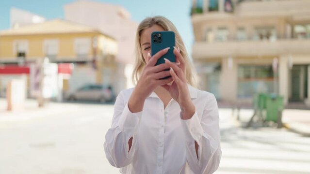 Young blonde woman making picture by the smartphone at street