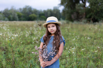  Cute girl in a hat in a field. Kid girl 4-5 year old wearing  hat  outdoors. Looking at camera.