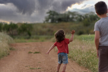 Fototapeta premium Two Caucasian boys walk through the field looking at a storm in the sky.