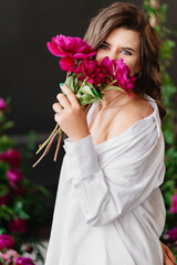 Fototapeta na wymiar A gentle and happy brunette woman in white clothes with a bouquet of peonies.
