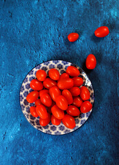Cherry tomatoes on a plate. Blue textured background with copy space.  Eating healthy concept. 