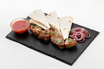 Pita with beef skewers and sauce and round onions on a black stone background and white background