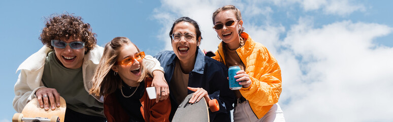 low angle view of excited multiethnic skaters laughing outdoors, banner.