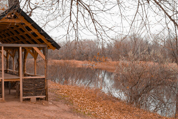 Autumn landscape with an empty wooden gazebo by the river in the forest. Nature park, recreation and relaxation area, outdoor walks. Blank for calendars and postcards, a place for text, copy space