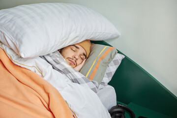 Teenager boy freeze at cold home, sleep on bed under warm blanket and pillow. Have problem with...