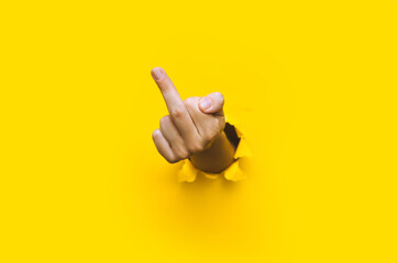 Middle finger of left hand, insulting gesture. Torn hole in yellow paper. Fuck you concept....