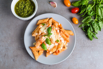 Penne pasta with tomato sauce and pesto with basil, cheese, garlic and tomatoes on a gray background.
