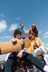 low angle view of young friends with skateboard and longboard against blue cloudy sky. © LIGHTFIELD STUDIOS