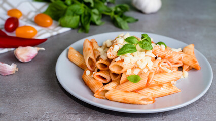 Pasta penne alla arrabiata with basil and cheese on gray background. Classic italian pasta penne with chili sauce arrabbiata.