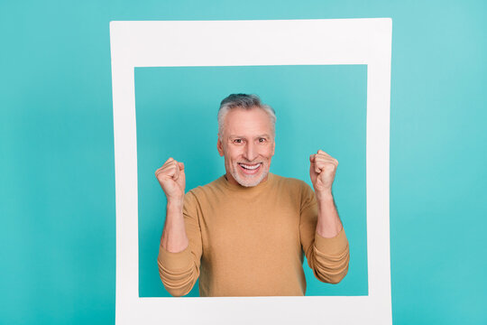 Portrait of delighted positive man raise fists success paper album card isolated on teal color background
