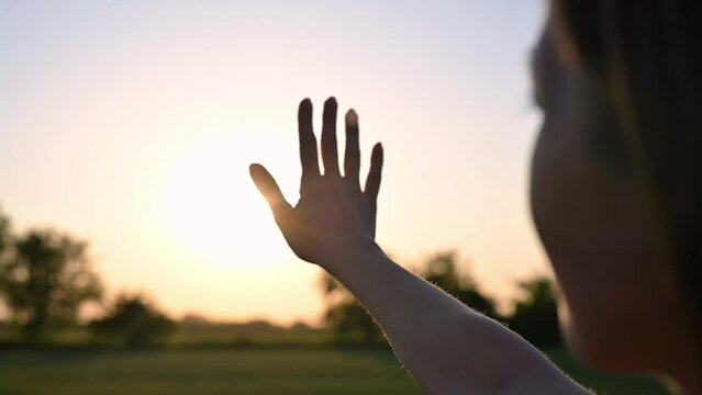 Young pretty girl catches the rays of the setting sun with her hands in field. Woman's hand at sunset close-up. Free meditating woman happy family dreams of happiness silhouette of hands. Slow motion