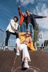 stylish woman in sunglasses near multiethnic friends on ramp in skate park.