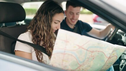 Young hispanic couple looking city map sitting on car at street