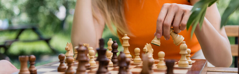 Cropped view of woman playing blurred chess in park, banner.