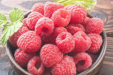Fresh appetizing raspberries in  bowl on a wooden table. close up