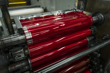 Magenta ink in the paint system compartment of a modern flexographic printing press in a print shop. Red paint in the ink feeder on the printing cylinder. Selective focus