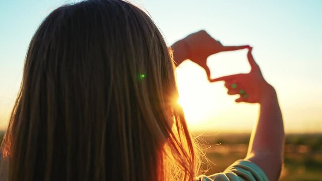 Silhouette young woman making frame around sun with her hands and catches rays of sun at sunrise on summer morning. Close up girl hands making frame gesture with sunset. Future planning in outdoor.