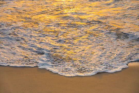 Close-up of calm ocean surf washing up onto beach at sunset