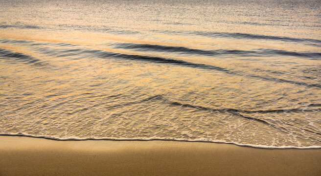 Close-up of calm ocean surf washing up onto beach at sunrise