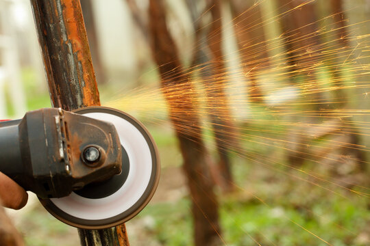 Close up of an angle grinder machine in motion, removing rust from an old metal construction outdoors with sparks flying