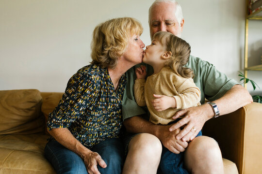 Grandmother kissing granddaughter (4-5) on sofa