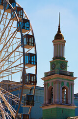 Obraz premium Scenic view of an ancient bell tower with clock at the blue sky background. The former Greek monastery. Ferris wheel in historical part of Kyiv. The Kontraktova Square. Kyiv, Ukraine