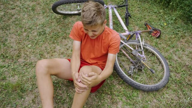 Agony from an injury when falling from a bicycle. Pain that is unbearable, a cry for help. The child screams in pain due to a leg injury. Sad tragedy with a young boy. The man is holding his knee