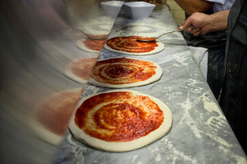 Man putting tomato sauce onto fresh hand made pizzas