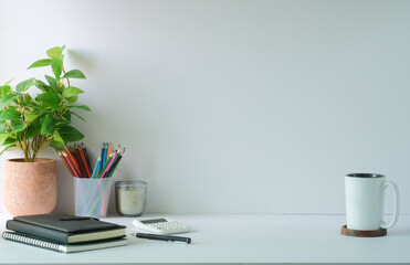 Creative workplace with potted plant, stationery, calculator and colourful sticky notes on light wall.