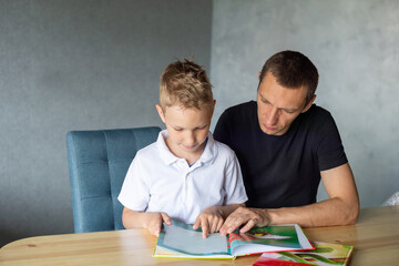 Naklejka premium A cute boy is sitting at the table with his dad and watching a book about snakes