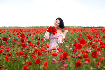 Naklejka premium A cute girl in a pink dress stands with a bouquet of poppies and smiles