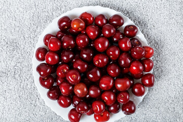 a lot of cherries in a white plate on a gray trendy background.