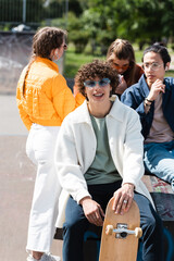 curly man with skateboard looking at camera near multicultural friends.