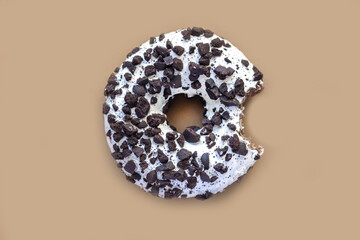 Glazed chocolate donut with bite missing on brown background