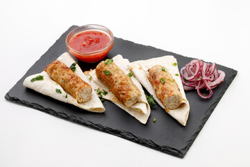 Pita with Sausage on it with round onion, sauce on a black stone background and white background