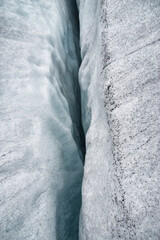 Long and deep crevasse on the Jostedalsbreen glacier in Norway in different shades of blue, white, and black color. A dramatic minimalistic scene for advertisement or desktop background.  