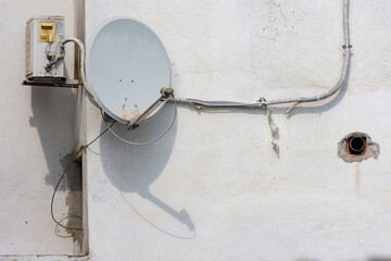 Signal receiver dish antenna installed on the exterior white wall for cable telecommunication