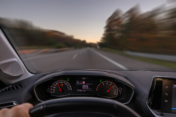 Driver view to the speedometer at 89 kmh or 89 mph and the road blurred in motion, night fall view from inside a car of driver POV of the road landscape.