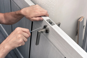 Man installs a doorknob on the door with a screwdriver. Screw tightening. Repair in the house.