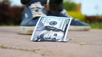 Close-up of one hundred dollar bill on the sidewalk and a man who found it