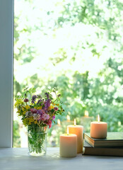 Beautiful meadow flowers in glass, candles and old books on wooden table, abstract green natural background. Summer season. floral composition in rustic style. reading, relax concept