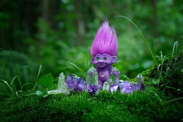 tale troll with crystals in forest, natural green background. troll toy with ruffled violet hair in mystery forest, symbol of fairytale.  - obrazy, fototapety, plakaty