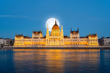 Amazing night view to Hungarian Parliament Building and Danube river with full moon over the city,...