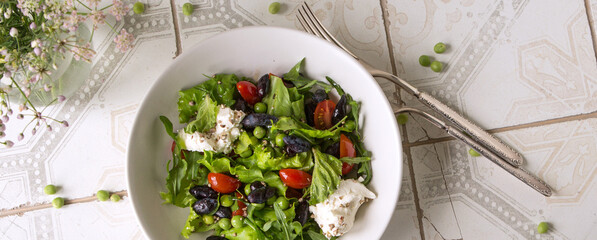 bowl with salad with greens, cherry tomatoes, green peas and honeysuckle on a light table
