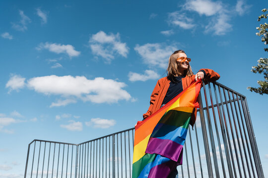 low angle view of smiling woman with lgbt flag against blue cloudy sky.