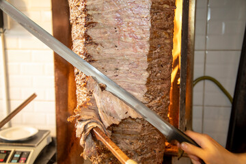 Doner meat being sliced from rotating spit - obrazy, fototapety, plakaty