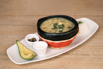 A bowl of Ajiaco served with capers and a slice of avocado